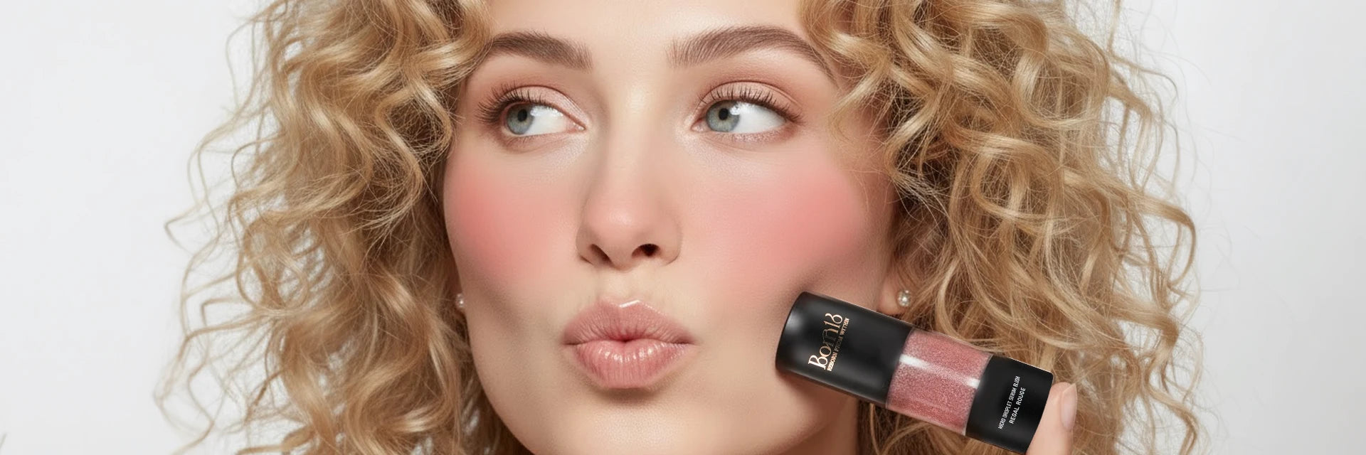 Beautiful woman with curly blonde hair and radiant dewy blush holding Born18 Micro Droplet Serum Blush. Natural flushed cheek look.